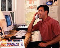 Imagem de um homem que trabalha no computador, falando no telefone