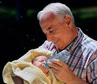 Imagem de um avô segurando seu neto recém-nascido, alimentando-o com uma garrafa